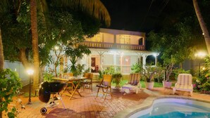 Ein gut beleuchteter Außenbereich mit Pool, Liegestühlen und Grill.