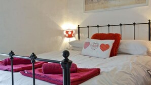 Una cama bien hecha con cabecera de metal negro, ropa de cama blanca y una manta roja.