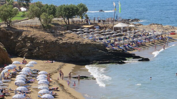 Una playa con sombrillas, gente y vistas al mar.