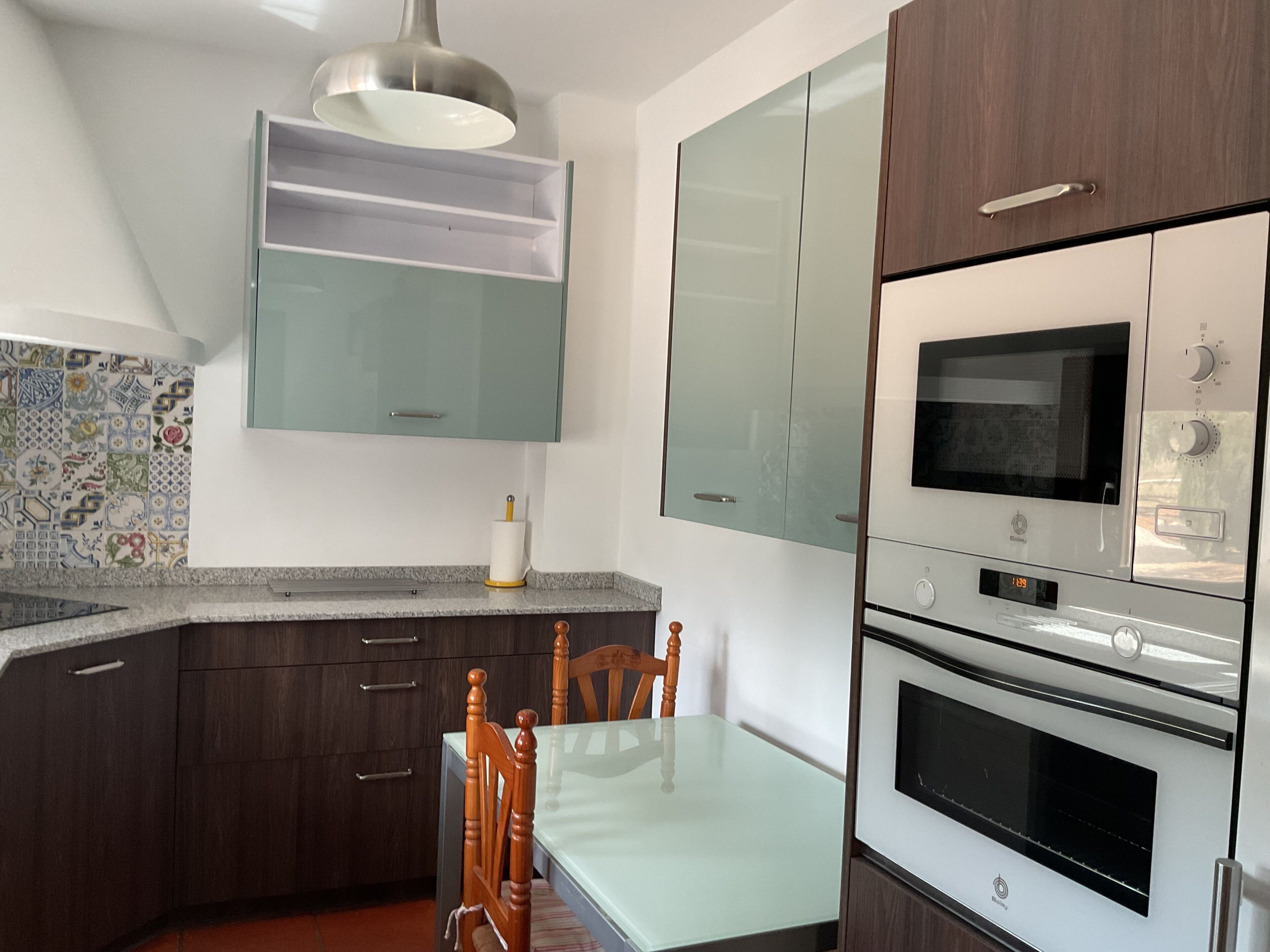 Uma cozinha com mesa, cadeiras, armários, micro-ondas e forno embutido.