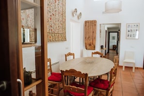 A dining area with a round table, wooden chairs with red cushions, a hanging tapestry, and a white chair. - RURAL HOUSE WITH PRIVATE POOL 4 KM FROM ROUND Wifi                         (Ronda)