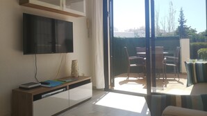 A living room with a flat-screen TV, a cabinet, and a sliding glass door leading to an outdoor patio with chairs and a table.