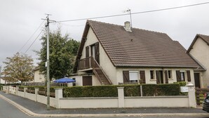 Una casa de dos pisos con techo inclinado, un balcón y un pequeño jardín.