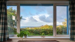 A room with a large window, a brown leather sofa, and a potted plant on the windowsill. - Beachside holiday home in stunning location overlooking the wild Atlantic way. (Castlecove)