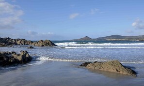 A rocky beach with waves, a clear sky, and distant mountains. - Beachside holiday home in stunning location overlooking the wild Atlantic way. (Castlecove)