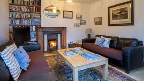 A cozy living room with a fireplace, leather sofas, a coffee table, and a bookshelf filled with books. - Beachside holiday home in stunning location overlooking the wild Atlantic way. (Castlecove)
