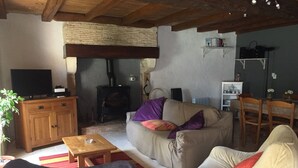 A cozy living room with a sofa, a wooden table, a television, and a fireplace. - The little chabrou cottage for 5 people  (Marillac-Le-Franc)