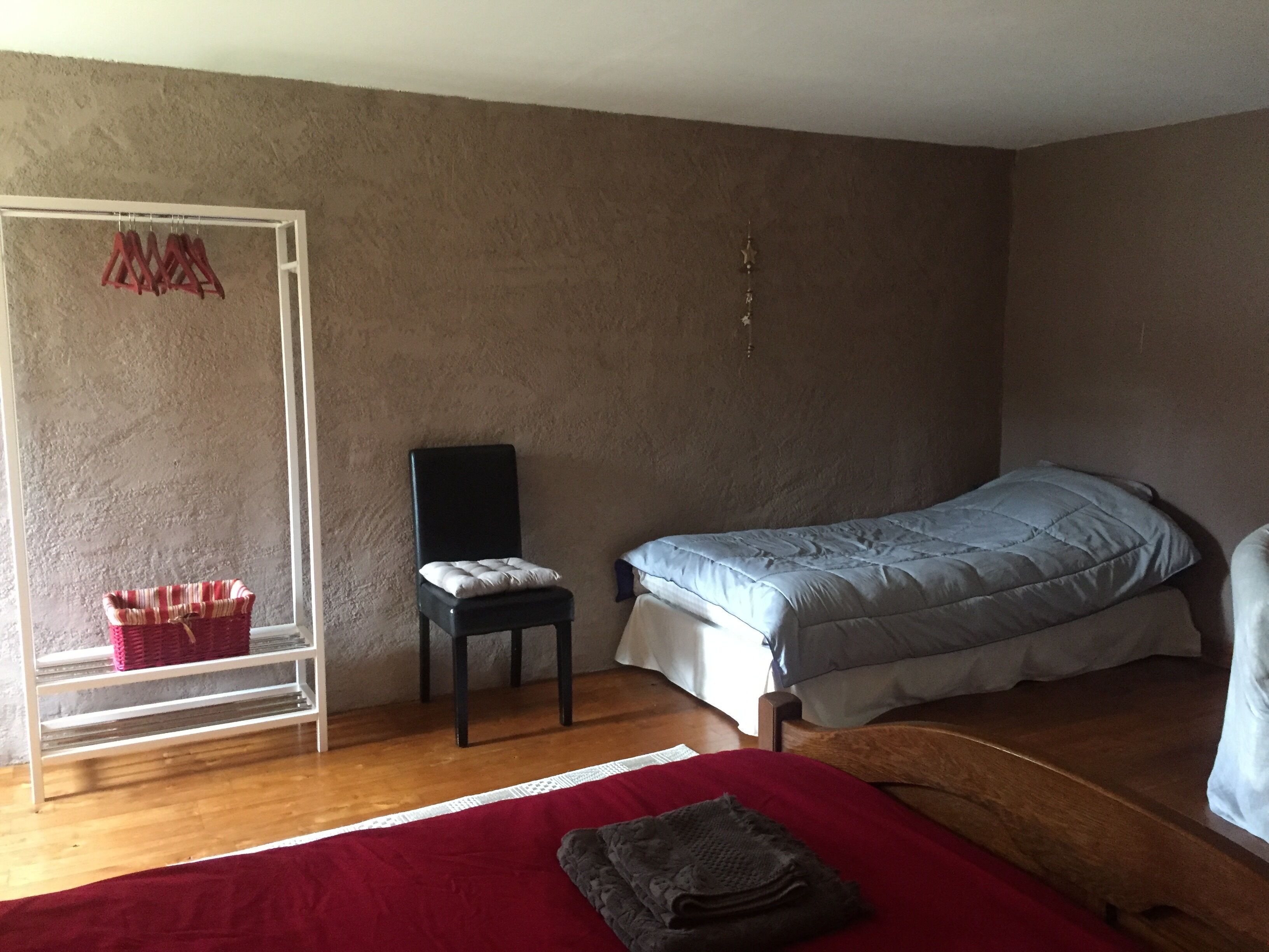 Een slaapkamer met een enkel bed, een stoel, een plank met kleding en een kledingroede.
