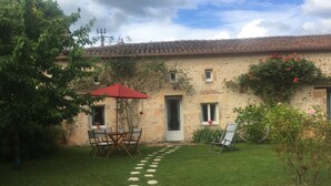 A stone building with a tiled roof, a small garden with a lawn, a red umbrella, and a seating area with chairs and a table. - The little chabrou cottage for 5 people  (Marillac-Le-Franc)
