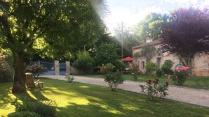 A well-maintained garden with a gravel path, a wooden chair, and a building with a red roof. - The little chabrou cottage for 5 people  (Marillac-Le-Franc)