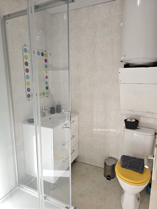 A modern bathroom with a glass shower enclosure, a white sink with a mirror, and a toilet with a yellow lid.