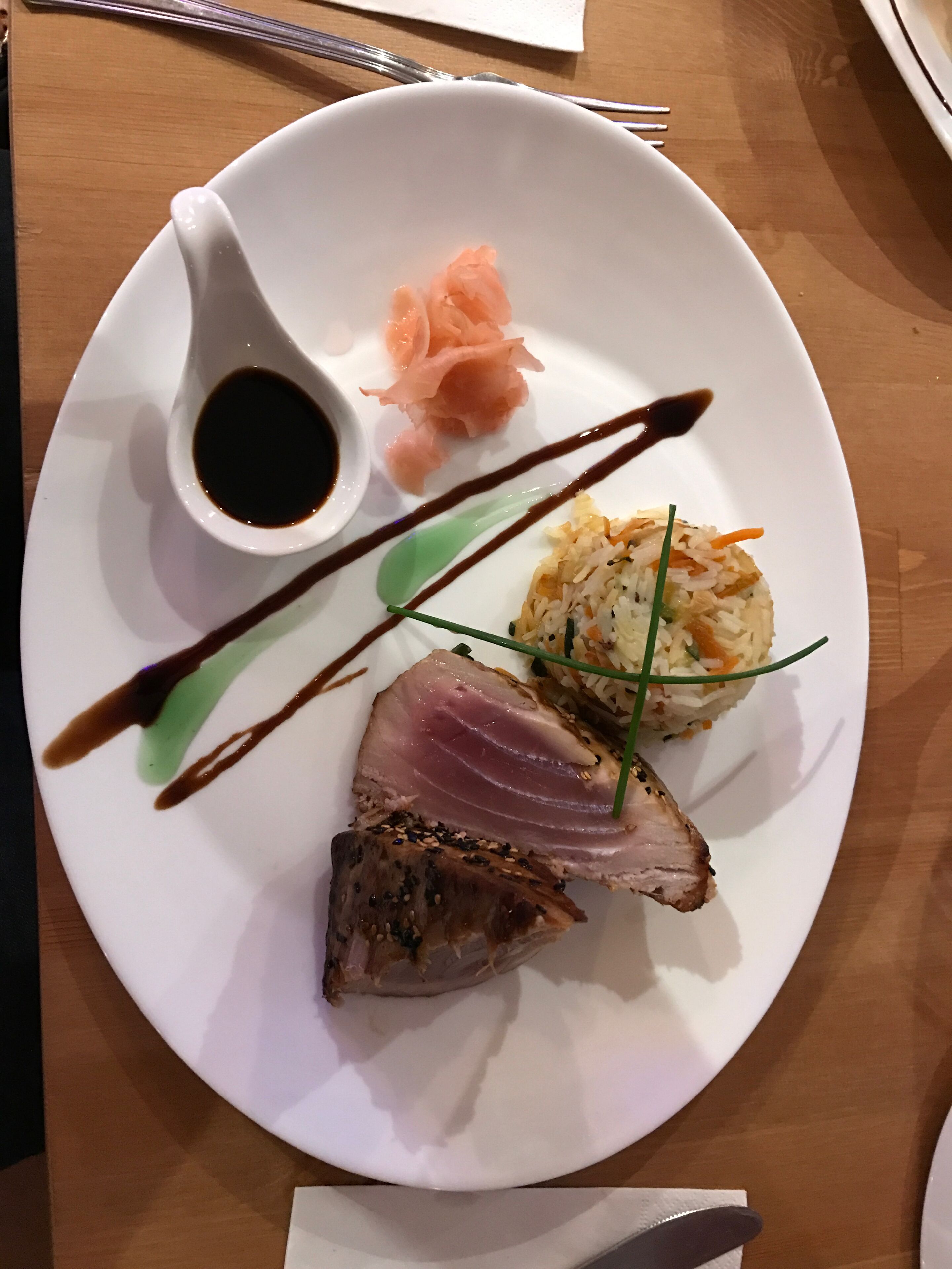A plate with a slice of meat, a small bowl of sauce, and a side of rice.