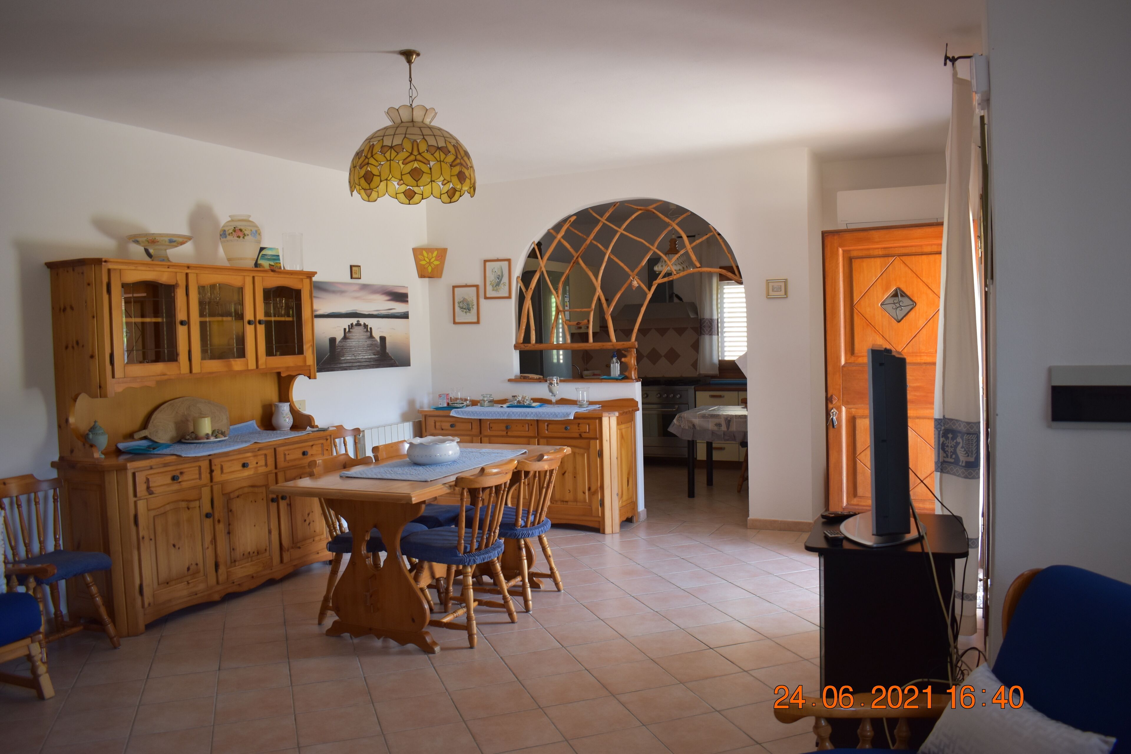 A dining area with wooden furniture, a chandelier, and a kitchen in the background.