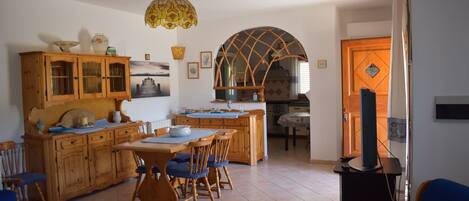 A dining area with wooden furniture, a chandelier, and a kitchen in the background.