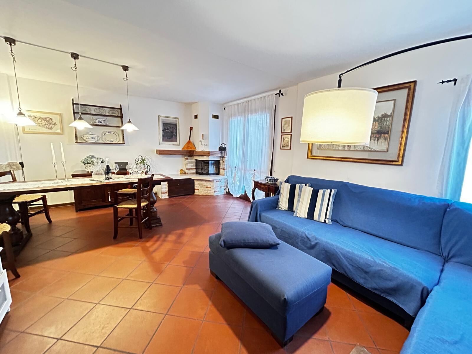 Ein Wohnzimmer mit blauem Sofa, einer Essecke mit Tisch und Stühlen sowie einer Küchenzeile mit Herd und Fenster.