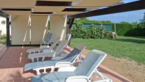 Ein überdachter Außenbereich mit weißen Lounge-Stühlen und einer Pergola.