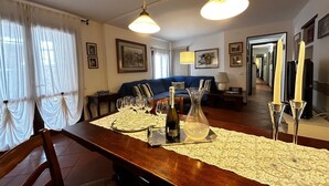 Ein Essbereich mit einem Holztisch, gedeckt für eine Mahlzeit, einer Couch im Hintergrund und einem Flur, der zu anderen Räumen führt.