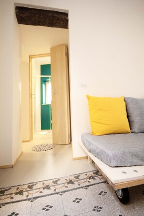 Une pièce avec un lit, un oreiller jaune, un oreiller gris, une porte en bois et un sol à motifs.