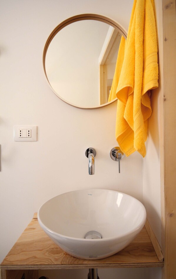 A bathroom with a white sink, a round mirror, and a yellow towel hanging on the wall. - for tourist use apartment: Textures tramari (Trapani)