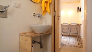 A bathroom with a white toilet, a wooden cabinet with a sink, a mirror, and two yellow towels hanging on the wall.