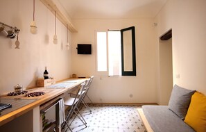 A compact kitchen with a wooden countertop, a dining table, and chairs. A television is mounted on the wall, and a window with a black frame is visible. - for tourist use apartment: Textures tramari (Trapani)
