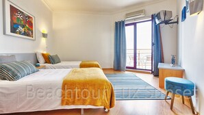 Ein Hotelzimmer mit zwei Betten, einem großen Fenster mit Vorhängen, einem kleinen Tisch und einem an der Wand befestigten Fernseher.
