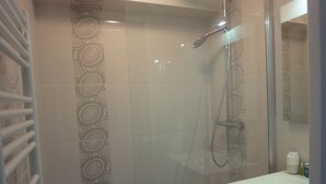 Eine Dusche mit Glastür, ein weißes Waschbecken und gemusterte Fliesen.