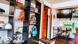 A room with a wooden floor, a television mounted on the wall, and a dining area with chairs and a table.