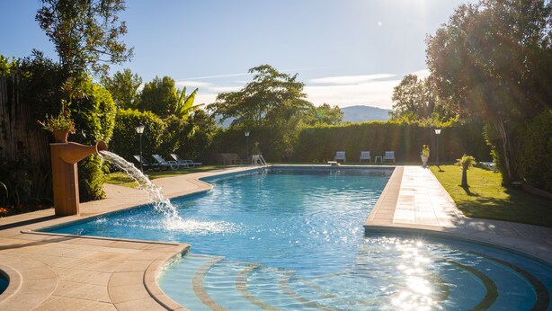 A swimming pool with a water feature, surrounded by lounge chairs and greenery.