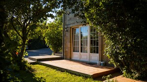 A building with a stone facade, large glass windows, and a wooden deck leading to a door.