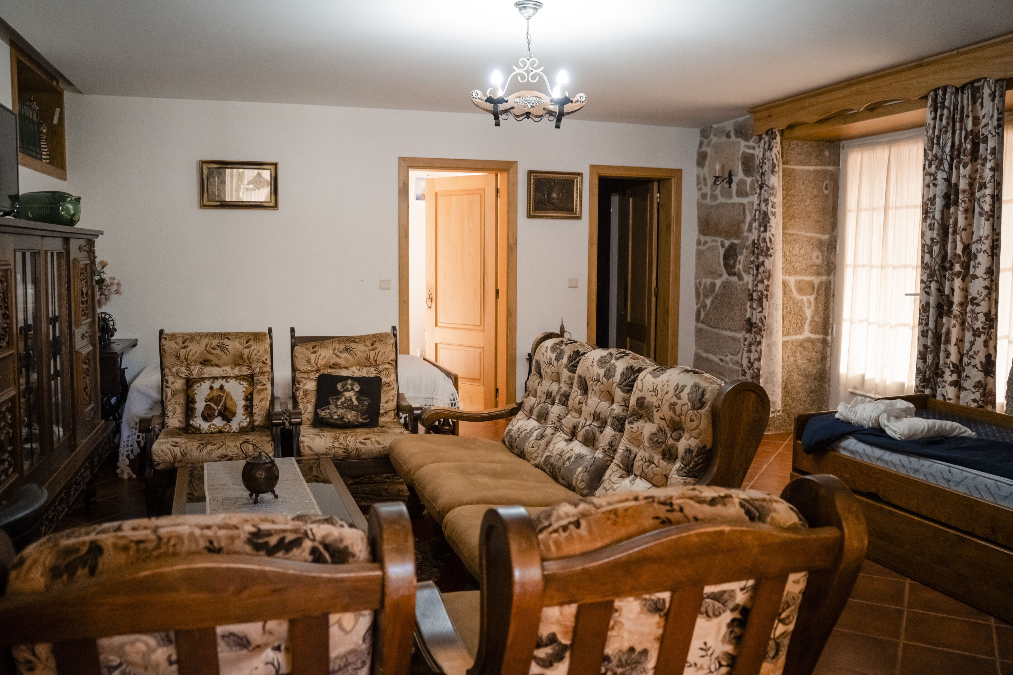 A cozy living room with a sofa set, wooden chairs, a table with a teapot, and a stone wall.