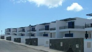 A row of modern, multi-story buildings with balconies, white exteriors, and a clear sky.