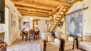 Un salon chaleureux avec un plafond en bois, un escalier, un coin repas et un ensemble de canapés.