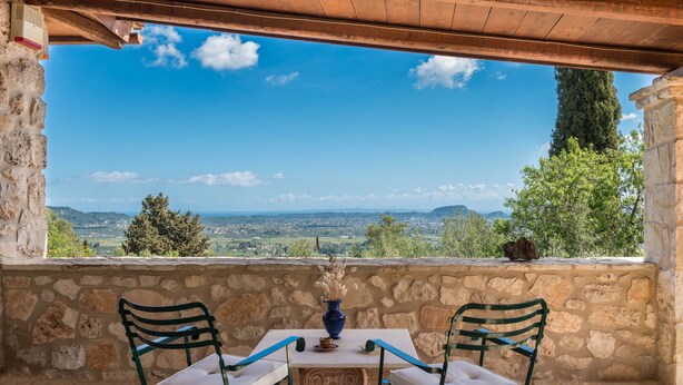Un balcon aux murs de pierre, agrémenté d’une table et de deux chaises, offrant une vue sur un paysage pittoresque.