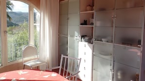 Quarto com uma janela grande, uma mesa de jantar, uma cadeira e um guarda-roupa com portas de vidro.