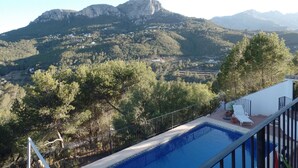 Piscina com vista para a montanha, rodeada por árvores e um edifício branco com varanda.
