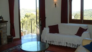 Uma sala de estar acolhedora, com um sofá branco, uma mesa redonda pequena e vista para uma varanda com guarda-corrimão.