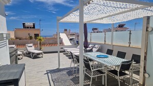 A rooftop terrace with lounge chairs, a table, and a pergola providing shade.