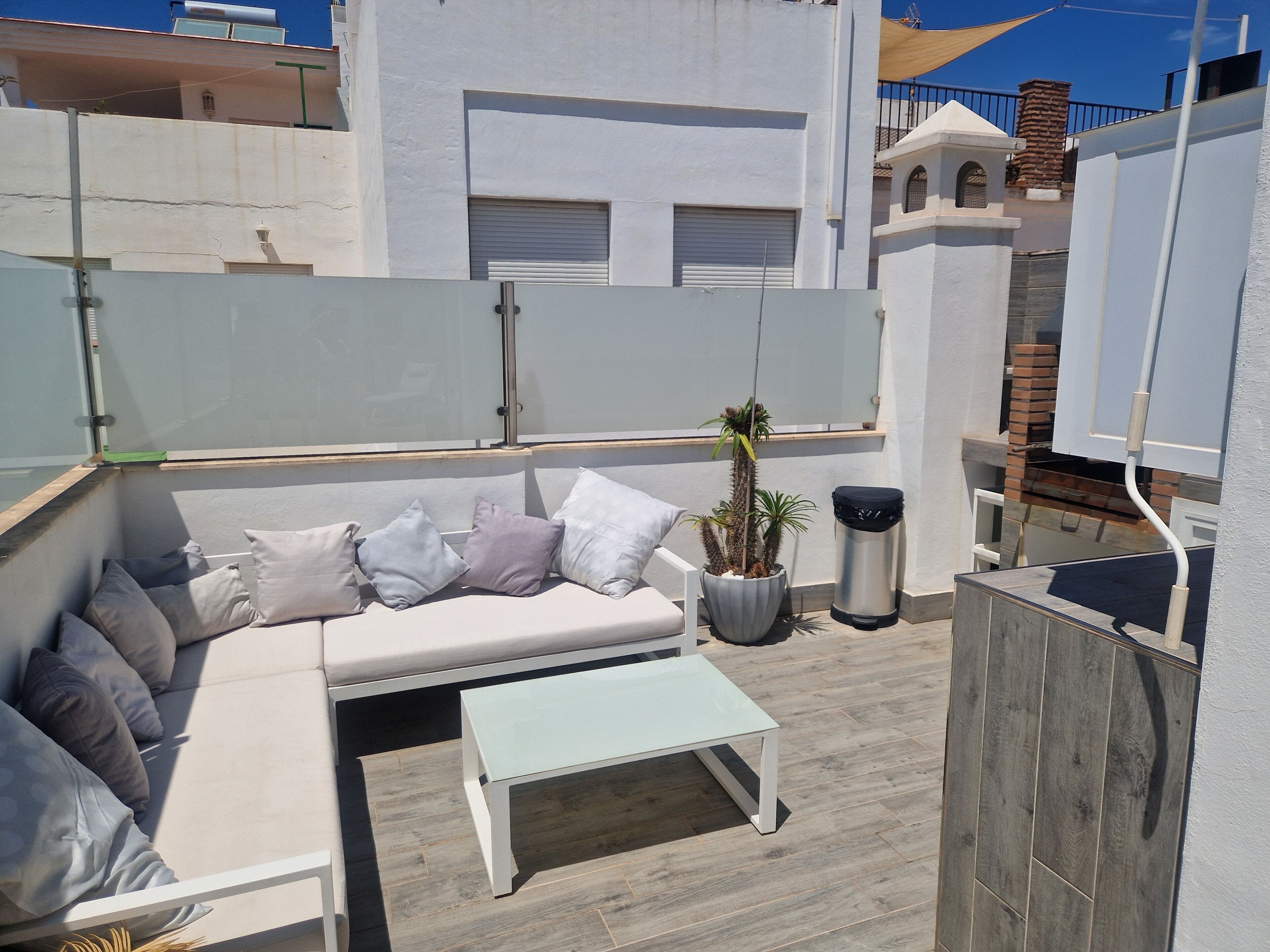A rooftop terrace with a white sofa, a small table, and a potted plant.