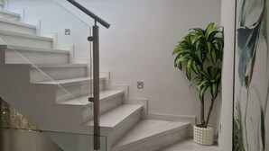 A modern staircase with a glass railing, a potted plant, and a painting on the wall.