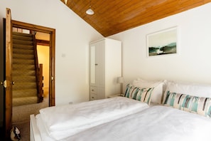 A bedroom with a wooden staircase, a bed with white linens, a nightstand, a lamp, and a painting on the wall.