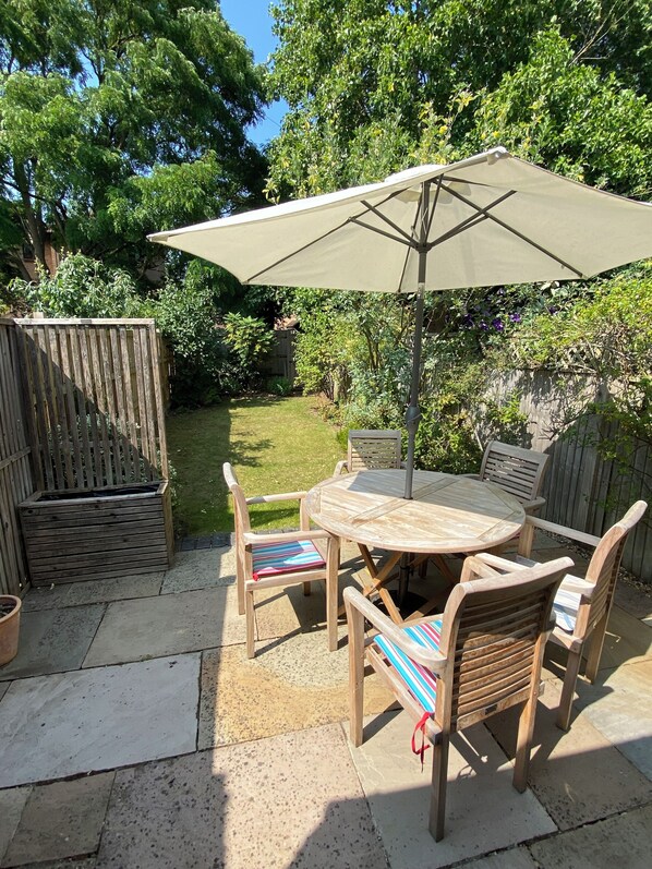 Une terrasse extérieure avec une table ronde, quatre chaises et un grand parasol.