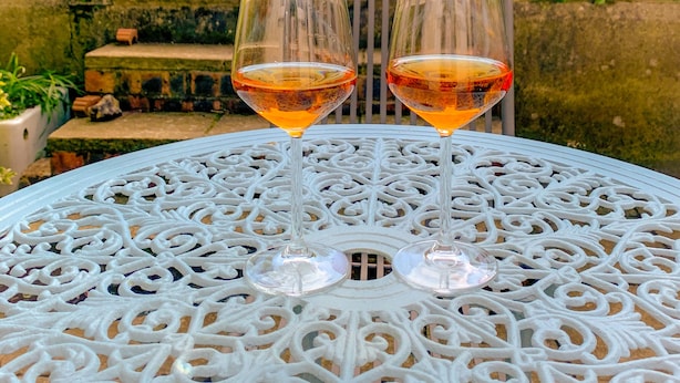 Two wine glasses on a white ornate table with a garden view in the background.