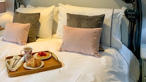 A neatly made bed with a tray of breakfast including croissants, a cup of coffee, and a plate of berries.