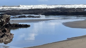 A beach with calm waters, rocky outcrops, and a clear sky.