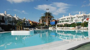 Ein Pool, umgeben von Liegestühlen und Palmen, mit Gebäuden im Hintergrund.