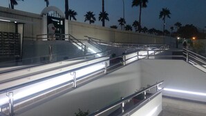 Eine moderne Außentreppe mit Metallgeländern und Glasverkleidungen, umgeben von Palmen und einem Gebäude mit einer gewölbten Fassade.