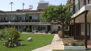 A courtyard with a grassy area, a pathway, and a building with multiple balconies and a covered seating area. - Dream holiday in Carihuela (Torremolinos)