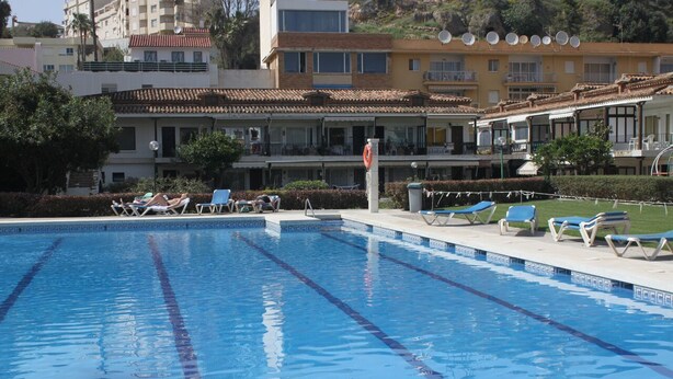 A swimming pool with lounge chairs and a view of residential buildings in the background. - Dream holiday in Carihuela (Torremolinos)