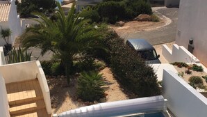 A pool area with a view of the sea, surrounded by greenery and buildings.